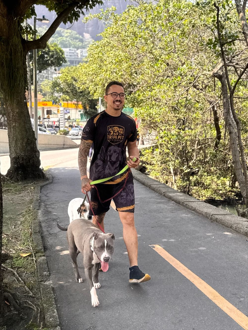 Jordan sorrindo durante o passeio, com a camisa da Tropa Pet e dois cães na guia