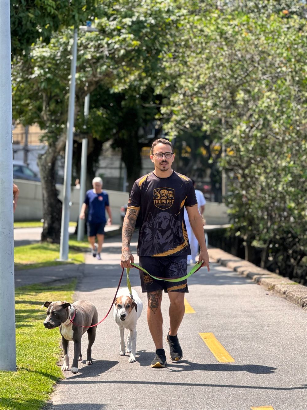 Jordan caminhando na ciclovia com dois cães na guia, com a camisa da Tropa Pet