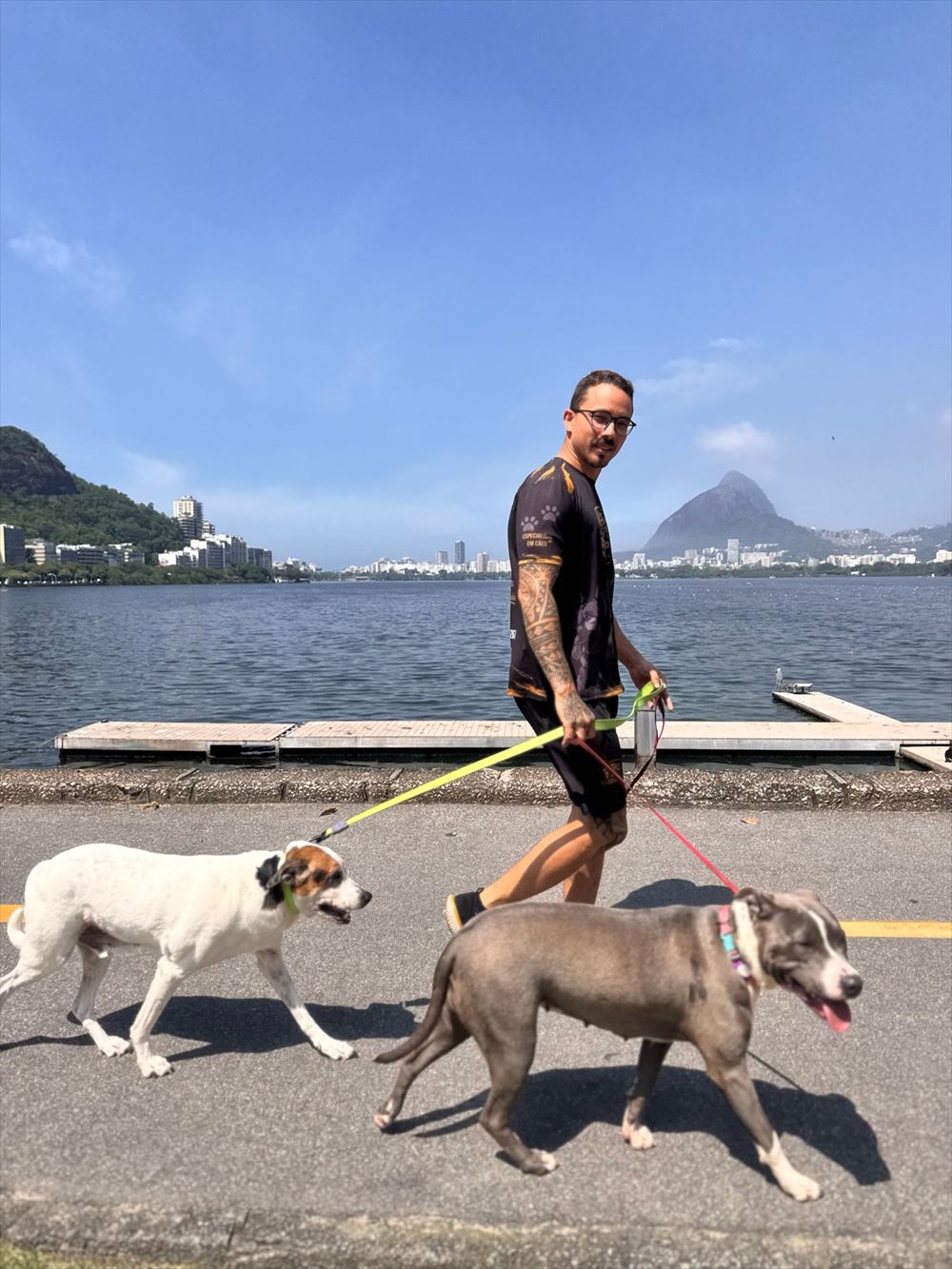 Jordan passeando com dois cães na beira da Lagoa, com o Morro Dois Irmãos ao fundo